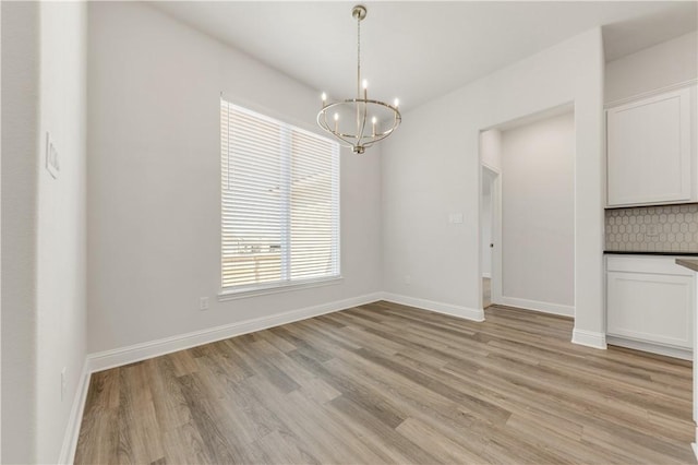 unfurnished dining area featuring light wood-style flooring, baseboards, and an inviting chandelier