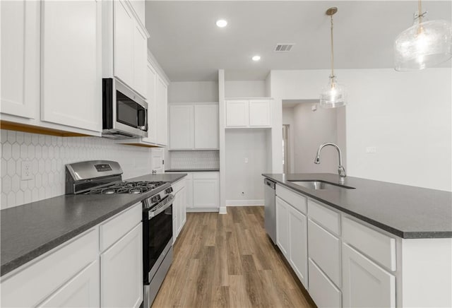 kitchen with visible vents, a sink, appliances with stainless steel finishes, dark countertops, and backsplash