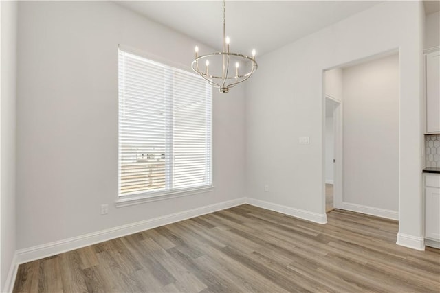 unfurnished dining area with baseboards, a chandelier, and light wood finished floors