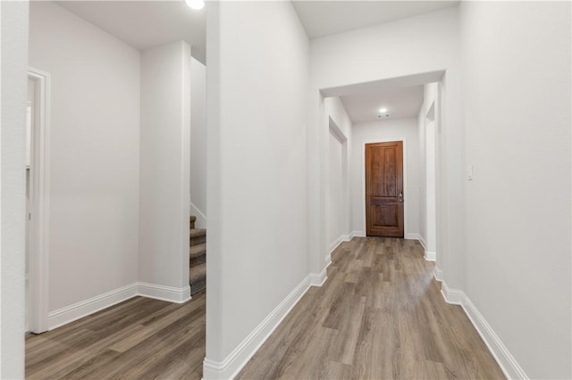 corridor with stairway, light wood-style floors, and baseboards