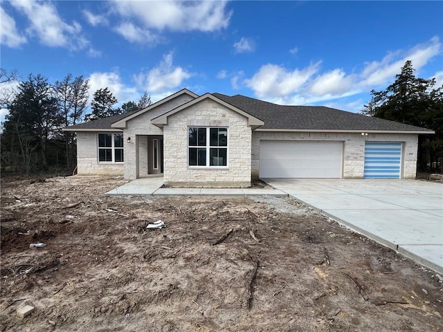 view of front of house featuring stone siding, concrete driveway, a garage, and roof with shingles