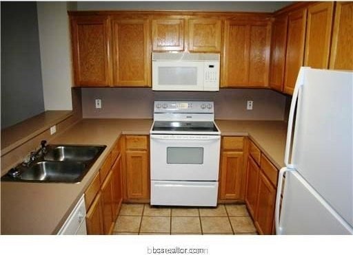 kitchen featuring a sink, light countertops, brown cabinetry, and white appliances