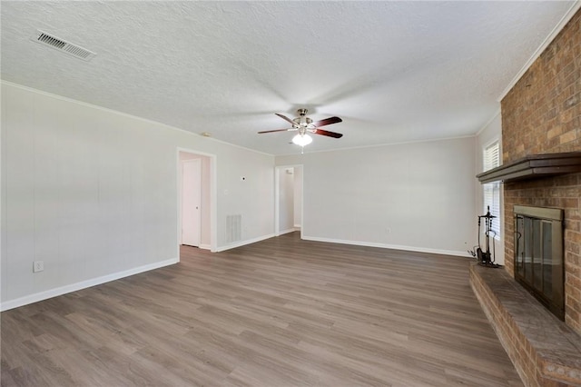 unfurnished living room with ceiling fan, a brick fireplace, hardwood / wood-style floors, a textured ceiling, and ornamental molding