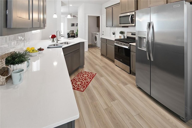 kitchen featuring appliances with stainless steel finishes, sink, light hardwood / wood-style flooring, washing machine and clothes dryer, and decorative light fixtures