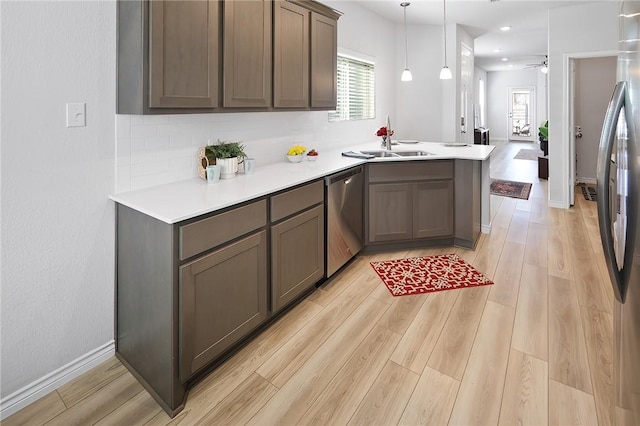 kitchen with sink, light wood-type flooring, stainless steel appliances, kitchen peninsula, and hanging light fixtures