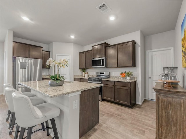 2412 Divot Ln, Navasota, TX 77868 - kitchen with appliances with stainless steel finishes, dark brown cabinetry, light stone counters, a breakfast bar area, and a kitchen island with sink