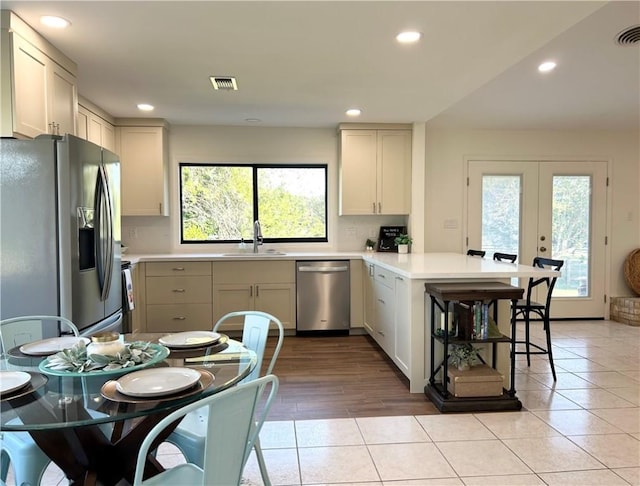 kitchen featuring stainless steel appliances, french doors, sink, kitchen peninsula, and light tile patterned floors