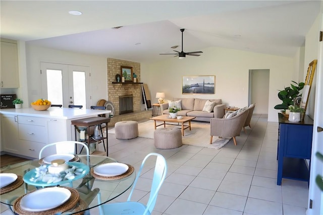 tiled dining space featuring ceiling fan, vaulted ceiling, french doors, and a fireplace