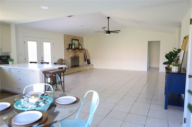 dining room featuring ceiling fan, vaulted ceiling, a fireplace, light tile patterned floors, and french doors