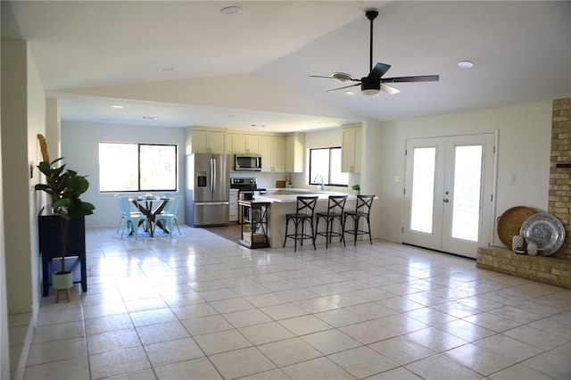 kitchen with appliances with stainless steel finishes, a kitchen breakfast bar, french doors, vaulted ceiling, and a center island