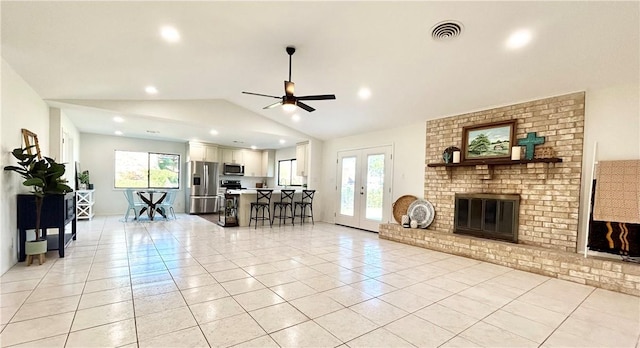 living room featuring lofted ceiling, ceiling fan, a fireplace, light tile patterned floors, and french doors