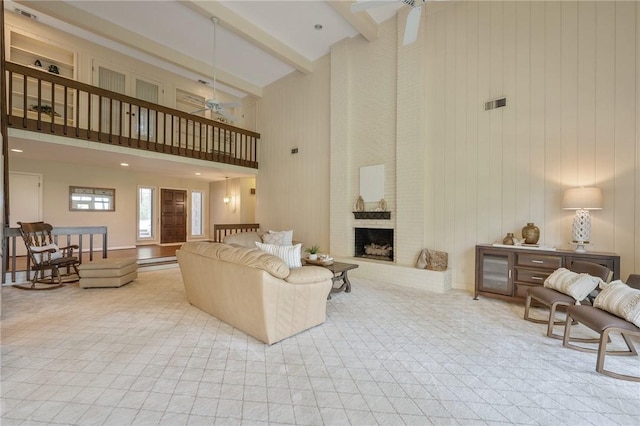 living room with beam ceiling, ceiling fan, a fireplace, and a towering ceiling