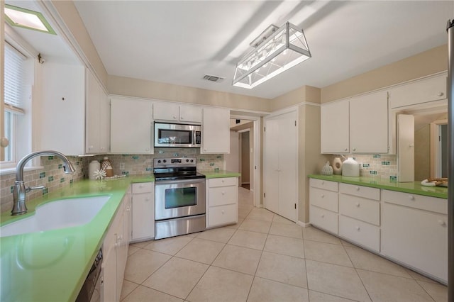 kitchen with white cabinetry, sink, stainless steel appliances, backsplash, and light tile patterned flooring