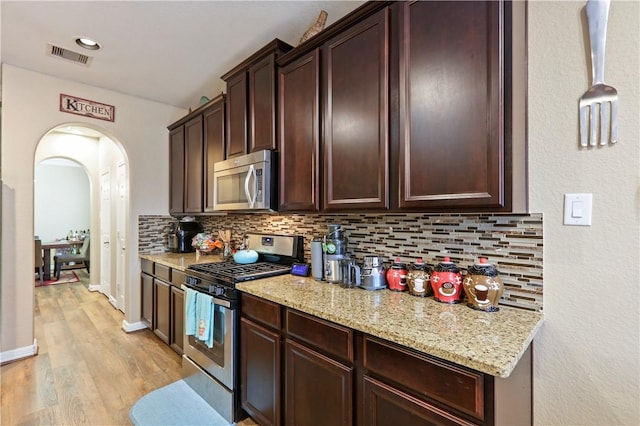 kitchen with pendant lighting, light stone countertops, appliances with stainless steel finishes, tasteful backsplash, and light hardwood / wood-style floors