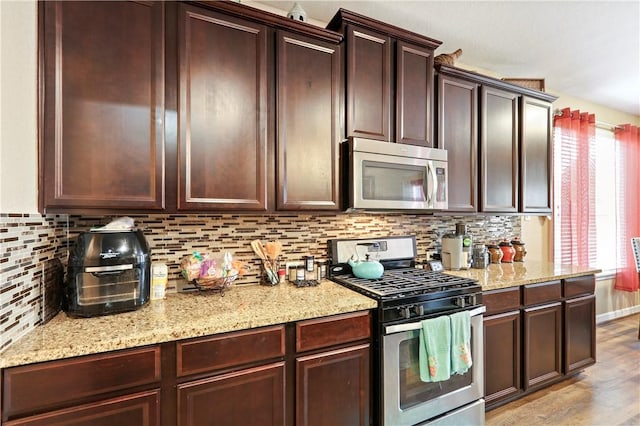 kitchen with light stone countertops, backsplash, appliances with stainless steel finishes, and light hardwood / wood-style flooring