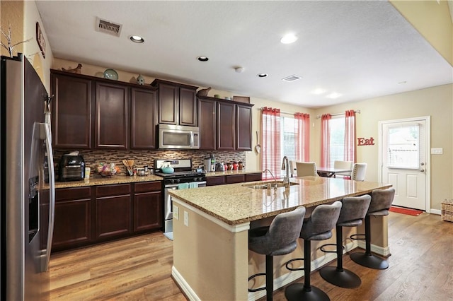 kitchen with sink, light hardwood / wood-style flooring, an island with sink, appliances with stainless steel finishes, and a breakfast bar area