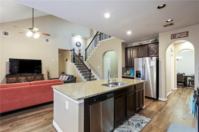 kitchen with appliances with stainless steel finishes, dark brown cabinetry, a kitchen island with sink, hardwood / wood-style flooring, and high vaulted ceiling