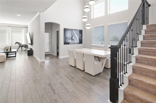 interior space featuring arched walkways, light wood finished floors, stairway, ornamental molding, and baseboards