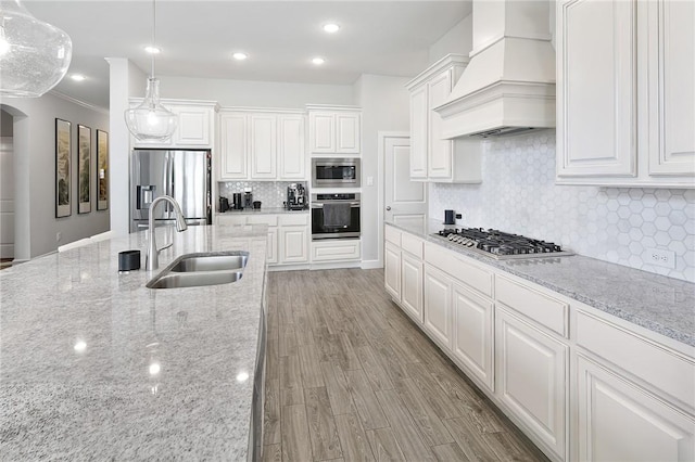 kitchen with arched walkways, a sink, white cabinetry, appliances with stainless steel finishes, and custom exhaust hood