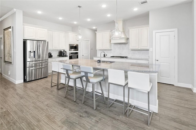 kitchen featuring custom exhaust hood, stainless steel appliances, light wood-style floors, white cabinetry, and a sink