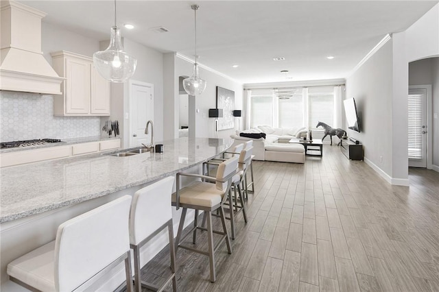 kitchen with stainless steel gas cooktop, tasteful backsplash, open floor plan, wood finished floors, and premium range hood