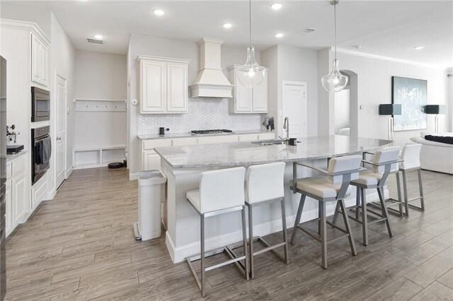 kitchen featuring appliances with stainless steel finishes, light wood-type flooring, a sink, and custom range hood