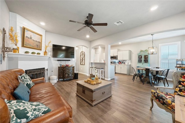 4143 Shallow Creek Loop, College Station, TX 77845 - living area with light wood-type flooring, ceiling fan, a glass covered fireplace, arched walkways, and recessed lighting