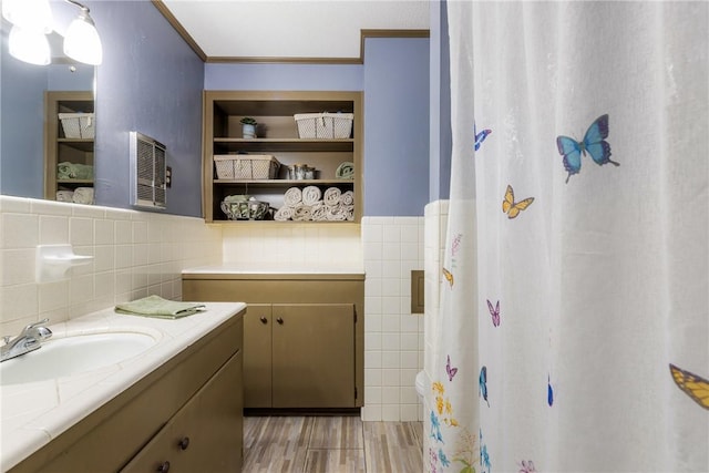 full bath featuring vanity, ornamental molding, wainscoting, wood finished floors, and tile walls