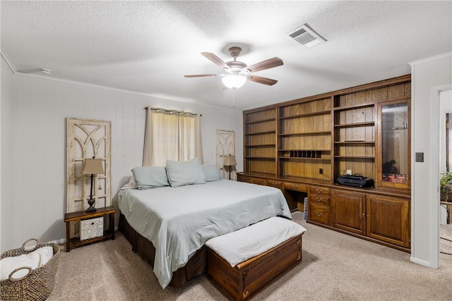 bedroom featuring visible vents, light colored carpet, built in desk, and a textured ceiling