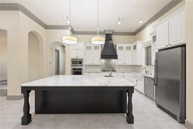 5217 Ruddy Duck Dr, College Station, TX 77845 - kitchen featuring appliances with stainless steel finishes, custom range hood, white cabinetry, a large island with sink, and light stone countertops