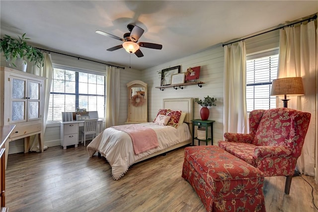 bedroom with wood-type flooring, multiple windows, wooden walls, and ceiling fan