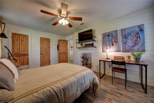 bedroom with ceiling fan, wood-type flooring, and wood walls