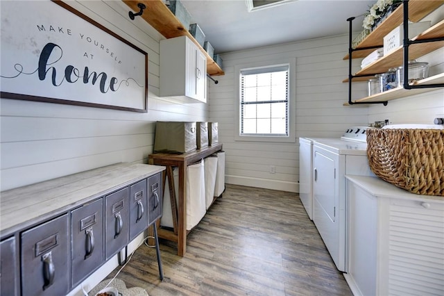 laundry room featuring washing machine and clothes dryer, wooden walls, cabinets, and wood-type flooring