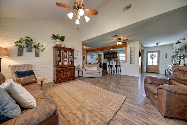 living room featuring wood-type flooring, high vaulted ceiling, ceiling fan, and wooden walls