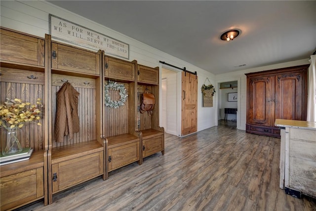 mudroom featuring a barn door, wooden walls, and dark wood-type flooring