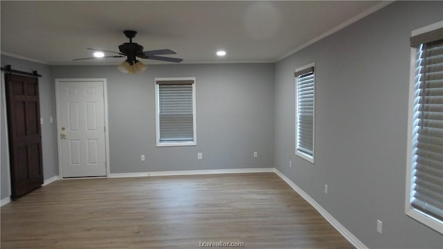 spare room featuring ceiling fan, a barn door, light wood-type flooring, and crown molding