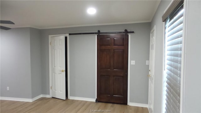 unfurnished bedroom featuring a barn door, crown molding, and light hardwood / wood-style floors