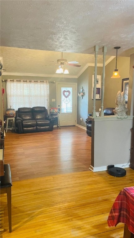 living room featuring hardwood / wood-style flooring, ceiling fan, crown molding, and a textured ceiling