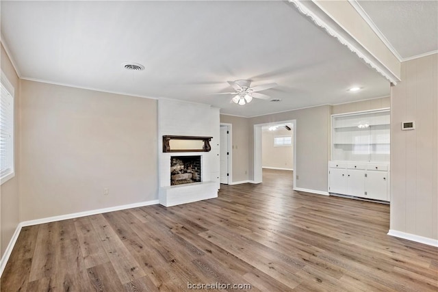 unfurnished living room featuring ceiling fan, ornamental molding, wood-type flooring, and a brick fireplace