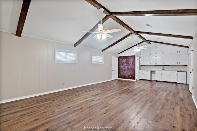 interior space with ceiling fan, sink, vaulted ceiling with beams, light hardwood / wood-style flooring, and wooden walls