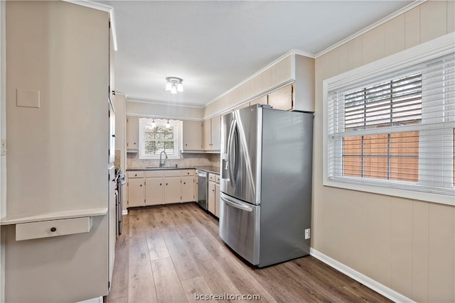 kitchen with appliances with stainless steel finishes, crown molding, sink, light hardwood / wood-style flooring, and wood walls