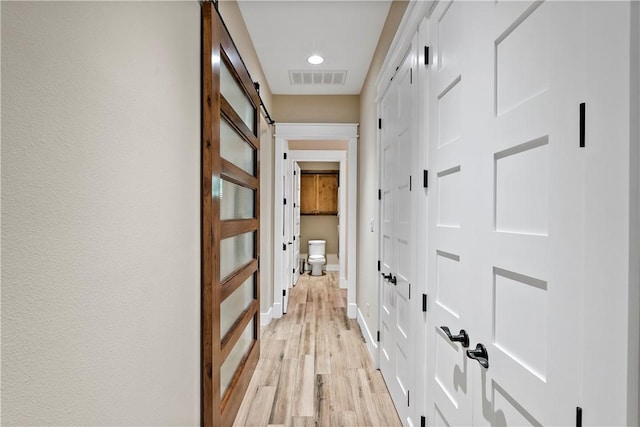 hallway with a barn door and light hardwood / wood-style flooring