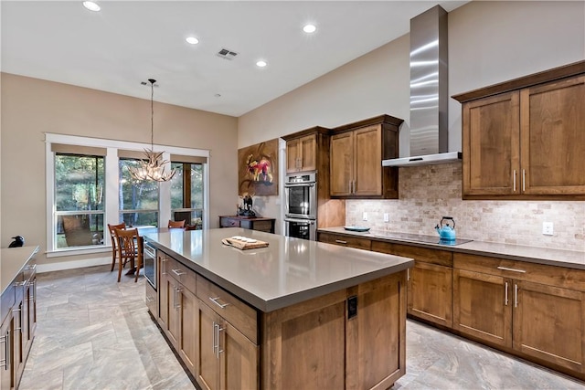 kitchen with wall chimney exhaust hood, stainless steel appliances, pendant lighting, an inviting chandelier, and a center island