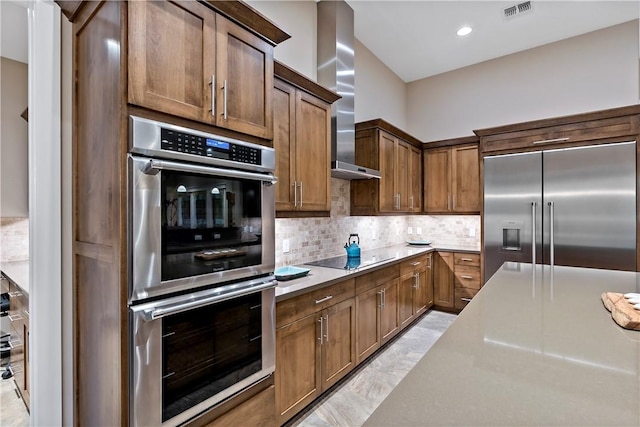 kitchen featuring decorative backsplash, light stone countertops, wall chimney range hood, and appliances with stainless steel finishes