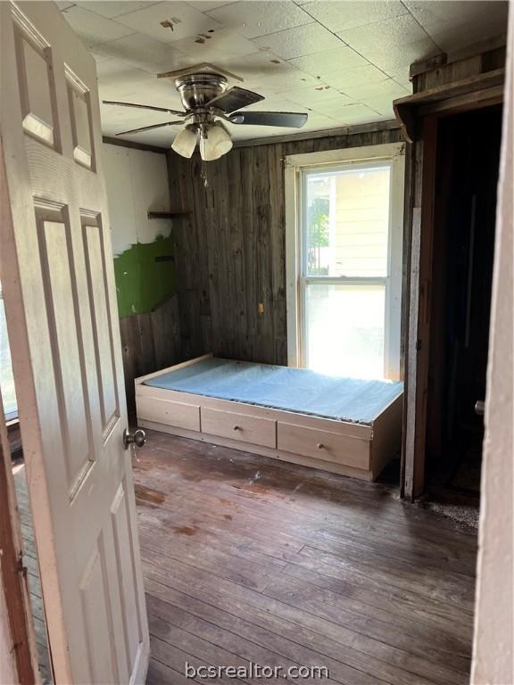 unfurnished bedroom featuring dark hardwood / wood-style flooring, ceiling fan, and wooden walls