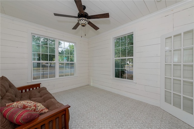 living area featuring ceiling fan, ornamental molding, and wooden walls