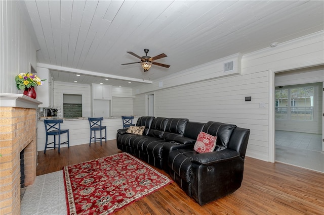 living room featuring a brick fireplace, ceiling fan, wooden ceiling, hardwood / wood-style floors, and wood walls