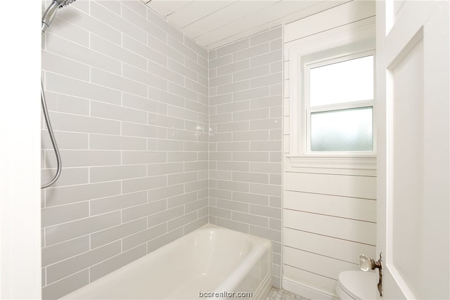 bathroom featuring toilet, tiled shower / bath, and wooden walls