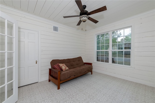 living area with ceiling fan, wooden walls, wood ceiling, and ornamental molding