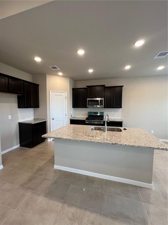 kitchen with light stone countertops, sink, an island with sink, light tile patterned floors, and appliances with stainless steel finishes